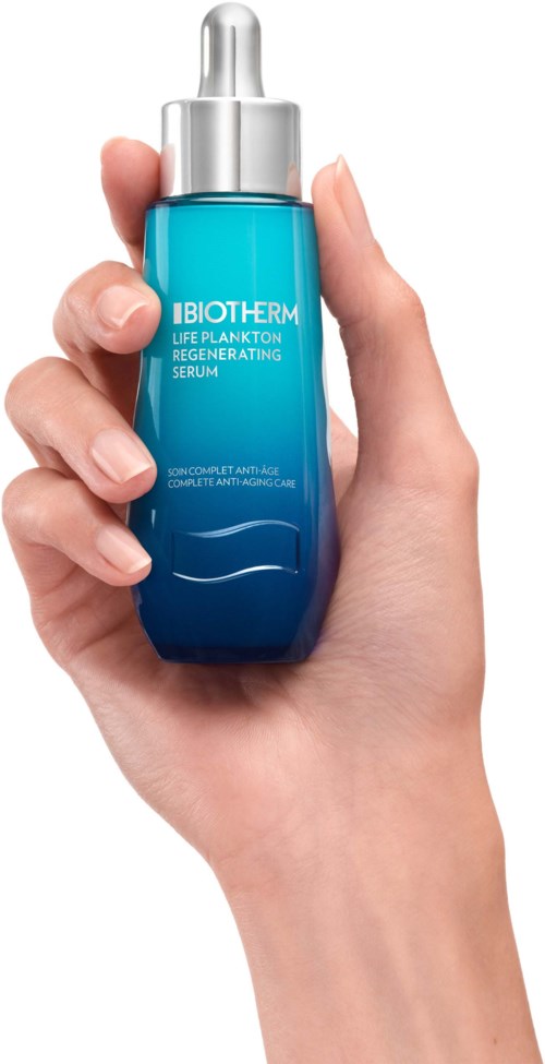 Een hand houdt een blauwe en zilveren serumfles met het label "IBIOTHER...SERUM."