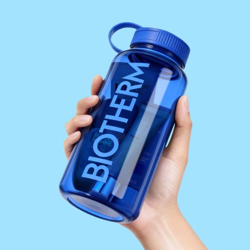 En hånd holder en blå beholder merket BIOTHERM mot en lys blå bakgrunn.