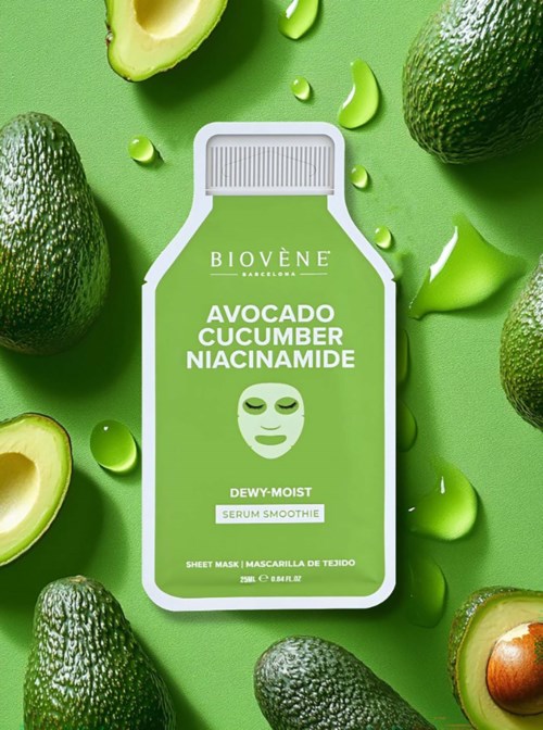 A facial mask package surrounded by avocados, cucumber slices, and green serum drops on a green background.