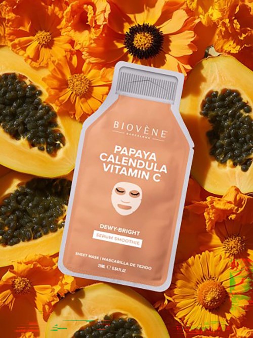 En ansiktsmask med papaya, ringblomma och vitamin C ligger bland papayabitar och ljusa orange blommor.