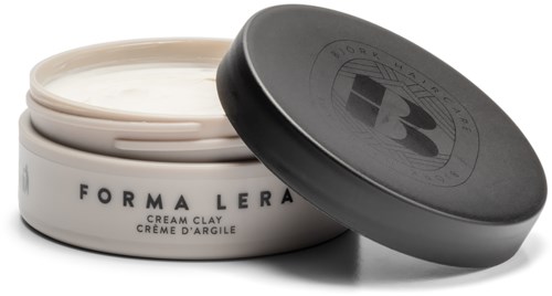 En burk med kräm med svart lock märkt 'Forma Lera' och 'Cream Clay', delvis öppen. Burken innehåller vit kräm.