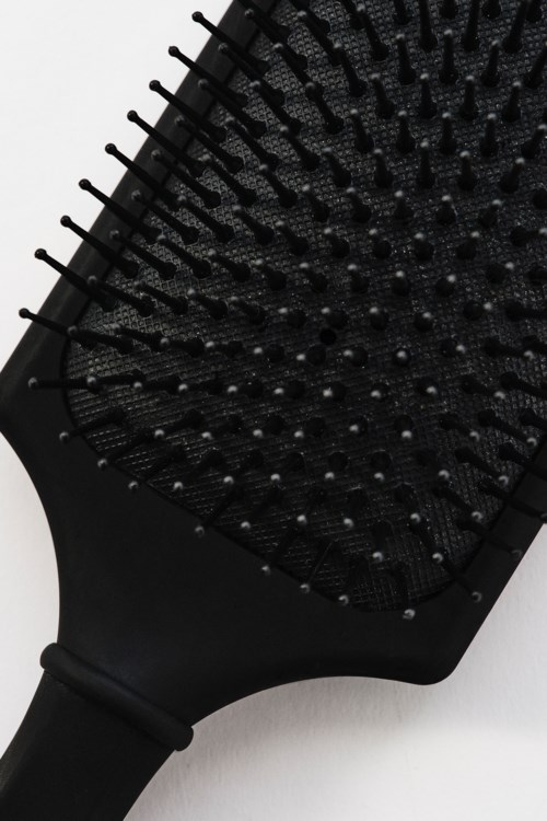 Eine schwarze Haarbürste mit langen, dünnen Borsten liegt flach auf einer weißen Oberfläche.