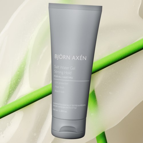 Eine graue Tube mit Björn Axén Salt Water Gel auf einer Oberfläche, mit einem grünen Stock und etwas weißer Flüssigkeit.