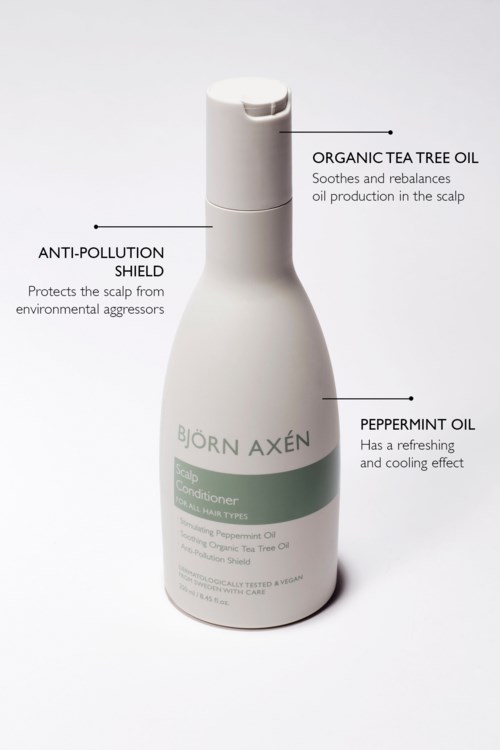 Een witte fles voor hoofdhuidverzorging met etiketten voor tea tree olie, pepermuntolie en bescherming tegen vervuiling.