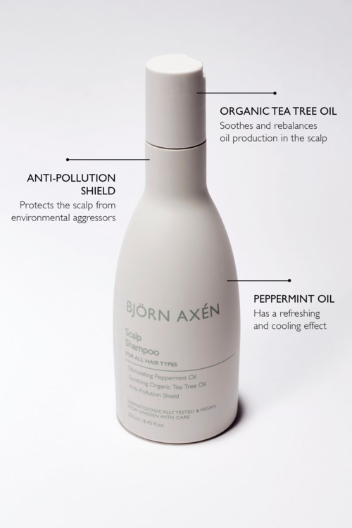 Een witte fles met Björn Axén haarproduct met labels voor tea tree olie, pepermuntolie en vervuilingsbescherming.