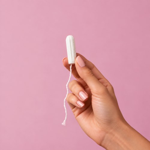 A hand holds a white tampon against a pink background.