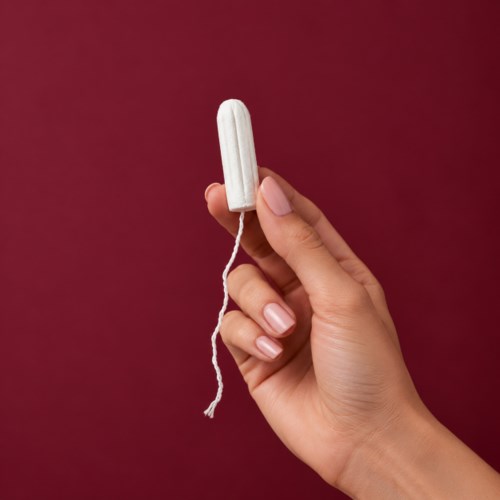 A hand holds a white menstrual cup against a red background.