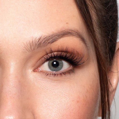 Close-up van een vrouw haar oog met lange wimpers, lichte huid en gedeeltelijk zichtbaar bruin haar.