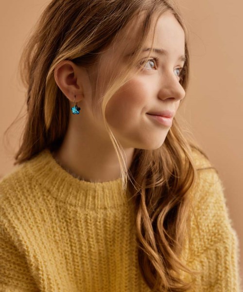 A young girl with long, wavy hair wearing a yellow knit sweater and star-shaped earrings, looking to the side.