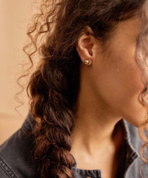 A woman with curly hair wearing a black jacket and gold earrings, partially visible from her right side.