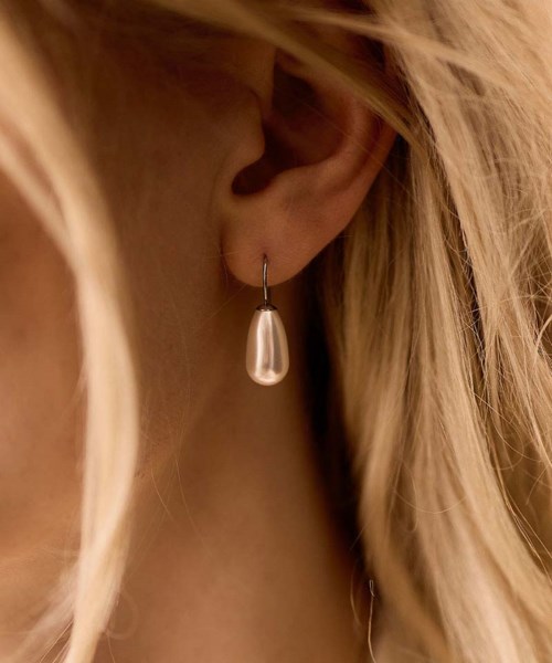 A woman wears a silver teardrop earring on her ear with blonde hair partially covering her face.