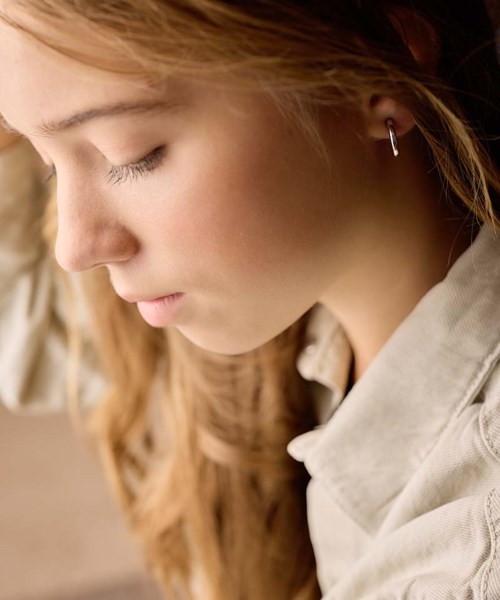 A young woman with closed eyes, long red hair, and silver earrings. She appears calm and introspective.