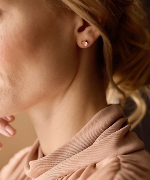 Close-up of a woman’s neck, ear with a small earring, and curled hair, wearing a beige top.