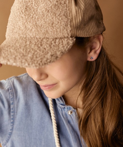En flicka med långt hår som bär en beige hatt och blå skjorta, ler lätt och tittar nedåt.