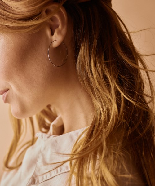 A woman with long, wavy red hair wearing a hoop earring and light-colored shirt, looking down indoors.