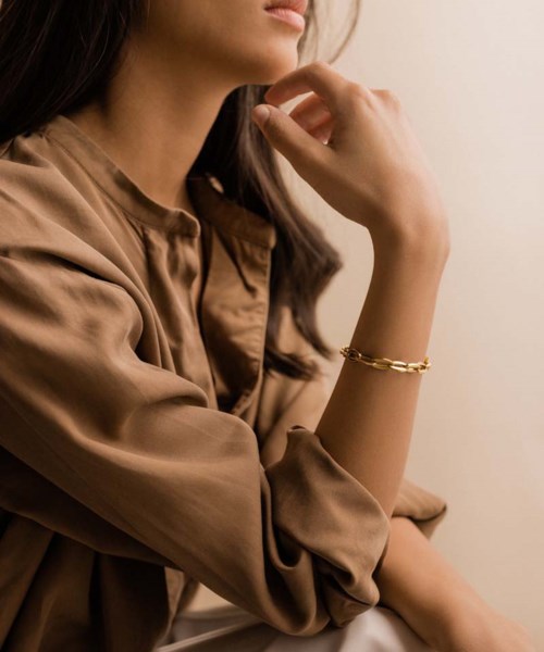 A woman wearing a brown satin shirt, gold bracelet, and resting her chin on her hand.
