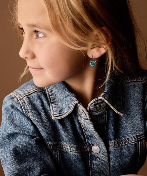 Side view of a girl wearing a denim jacket and blue earrings, looking to the left with a gentle smile.