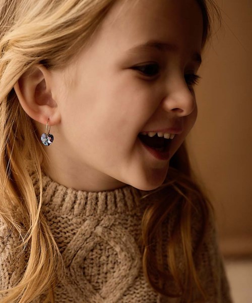 A girl with red hair wearing a brown knit sweater and sparkly star-shaped earrings, smiling and looking to her right.