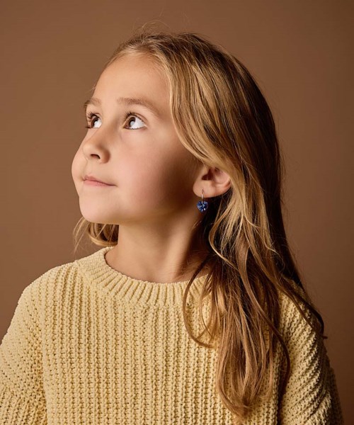 Young girl with long, wavy hair wearing blue earrings and a yellow knit sweater, looking to the side.