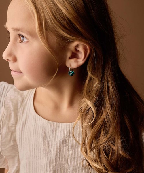 Profile of a young girl with long, wavy hair, silver earrings, and a gentle smile, facing left against a warm background.