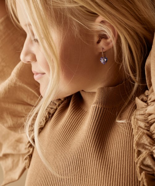 A woman with blonde hair is lying down, wearing a tan sweater and a heart-shaped earring.