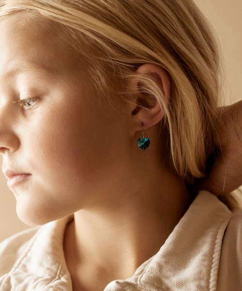 A girl with blonde hair and a blue heart-shaped earring looks to the side in soft light.