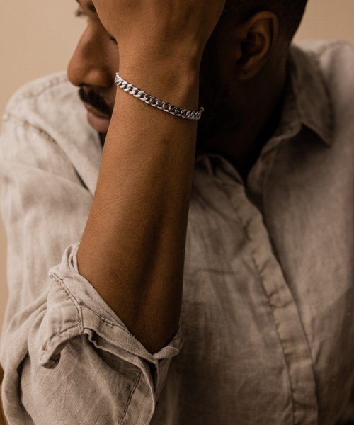 A person wearing a silver bracelet, with their face partially hidden, resting their head on their hand.