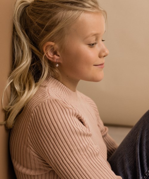 A young girl with blonde hair, smiling gently, sitting calmly with her eyes closed, wearing a pink sweater.