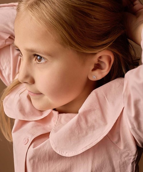 En ung flicka med rött hår i rosa jacka, tittar åt sidan med ett lugnt leende.