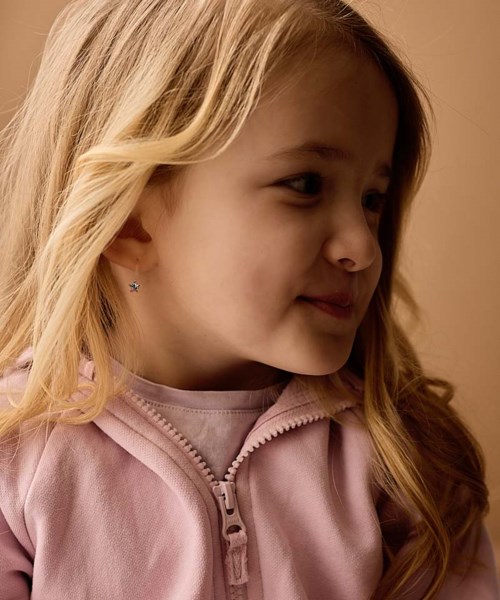 En flicka med långt blont hår som bär en rosa tröja med dragkedja, tittar åt höger med ett lugnt leende.