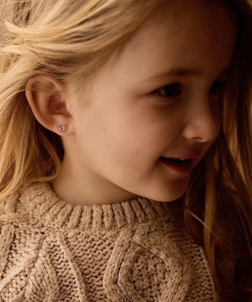 En ung flicka med blont hår, små örhängen och en beige stickad tröja, ler och tittar åt sidan.