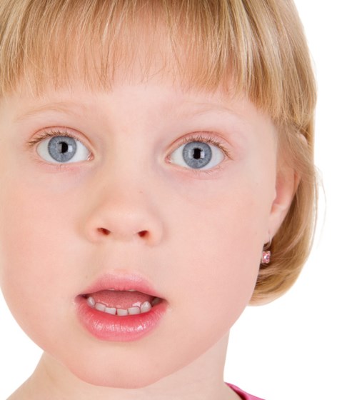 En ung jente med blå øyne og blond hår ser overrasket eller nysgjerrig ut. Hun har øredobber og litt åpne lepper.