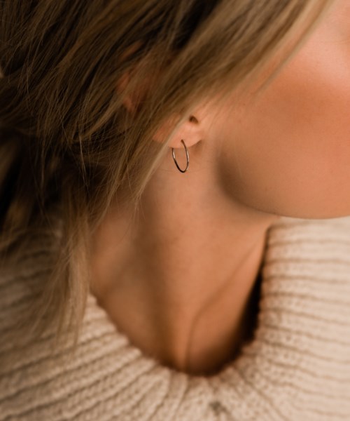 A woman wears a small hoop earring and a beige sweater. Her hair covers part of her face and shoulder.