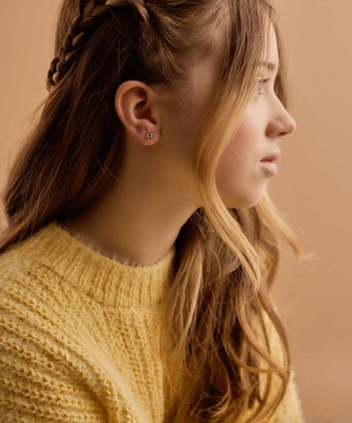 A young woman with long, wavy red hair, wearing a yellow knitted sweater, faces to the right. She has earrings and a calm expression.