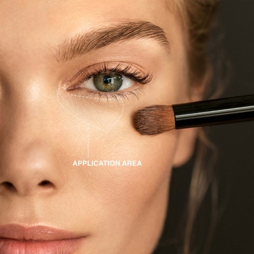Close-up of a woman's face showing her eye and cheek, with a makeup brush applying makeup near her eye.