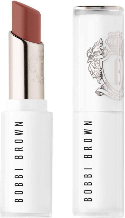A Bobbi Brown lipstick with a nude shade stands next to its clear cap with logo. The lipstick is in a white separate case.