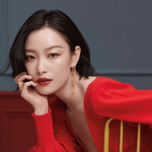 A woman with black hair in a red outfit poses confidently indoors.