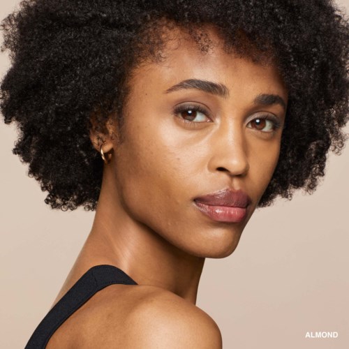 A woman with short, curly hair looking at the camera, with natural makeup and in a black top.