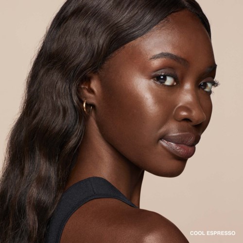 A woman with long brown hair, dark skin, and a confident expression, wearing a black top against a neutral background.