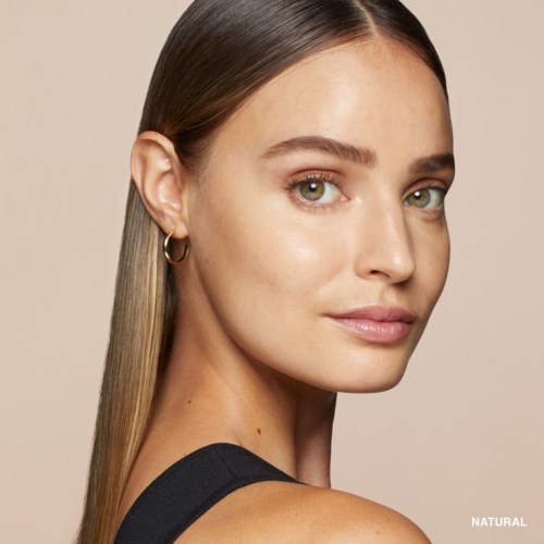 A woman with long hair and earrings, looking over shoulder with a slight smile, against a plain background.