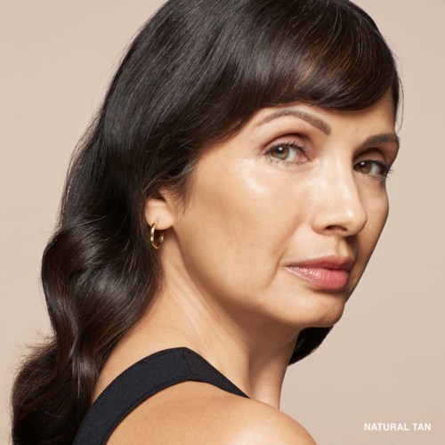 A woman with dark, wavy hair looking over her shoulder, wearing a black sleeveless top and small gold earrings.