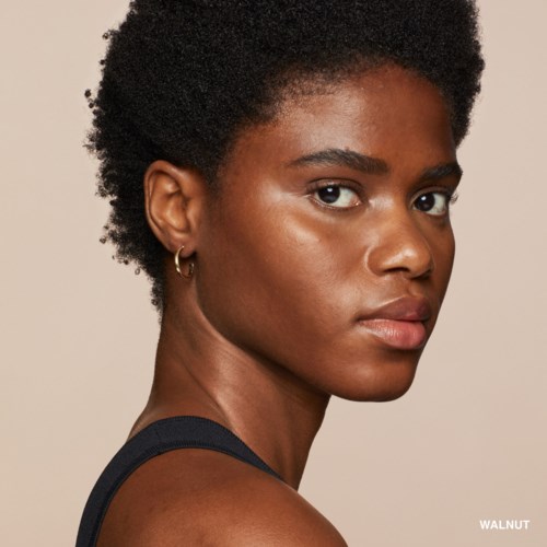 A confident woman with short curly hair, wearing a sleeveless top, looking sideways with a neutral expression.
