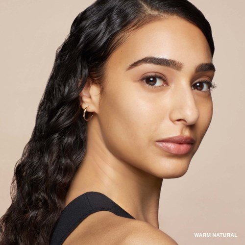 A woman with long, wavy black hair and light skin, looking over her shoulder with a calm expression.