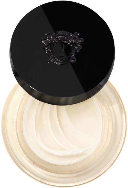 A round black lid with a silver emblem covers a cream-colored container filled with cream or moisturizer.