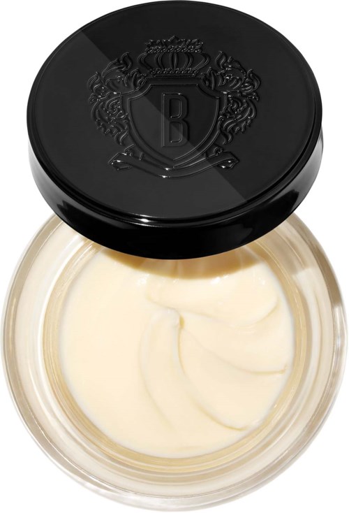 A small jar with a black lid that has a crest, filled with white cream or balm.
