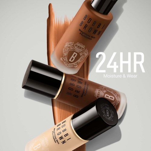 Three Bobbi Brown foundation bottles with different shades, lay on a light background with a smear of foundation in the same shades.