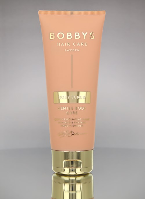 Rote Tube von Bobby's Hair Care Körperpeeling mit goldener Kappe und Text, auf grauem Hintergrund.