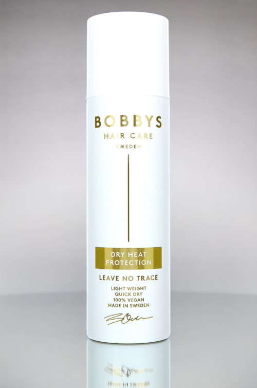 En hvit flaske med Bobby's Hair Care med gull- og svart tekst, mot en grå bakgrunn.