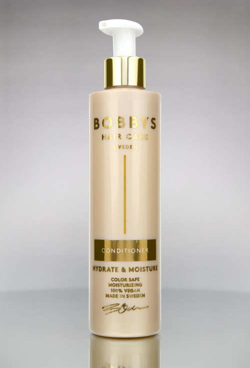 Een fles Bobby's Hair & Care Conditioner met goud en wit ontwerp, die haar hydrateert en verzorgt.