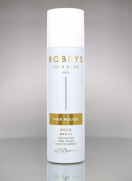 Eine weiße Flasche mit Gold- und Schwarzt text, gekennzeichnet als Bob Bys Hair Mousse für Halt und Volumen.
